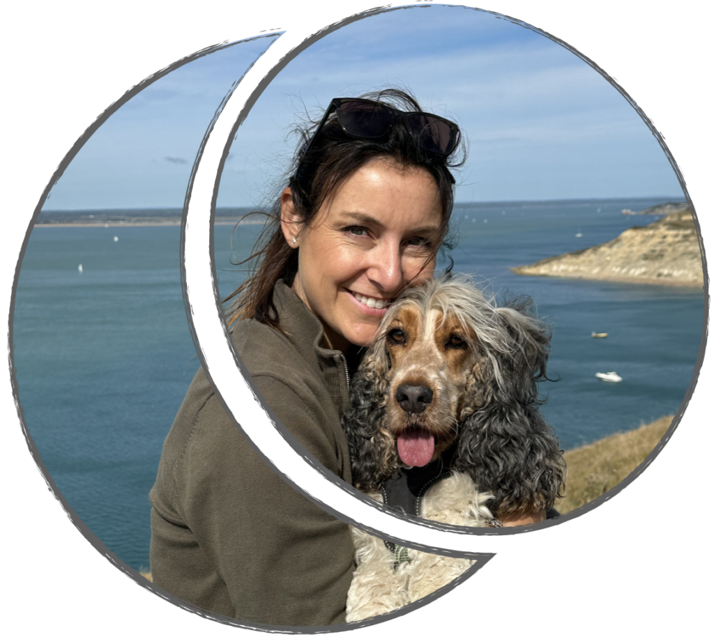 Ellie Kelland, owner of BARF time, smiling while hugging her grey eared, brown faced and white legs, rescue English Cocker Spaniel girl Brandy, who is also smiling with her tongue out. They are standing on a cliff overlooking the sea on a sunny day. The scene conveys warmth, love and happiness. There is a circular graphic that frames the photo.